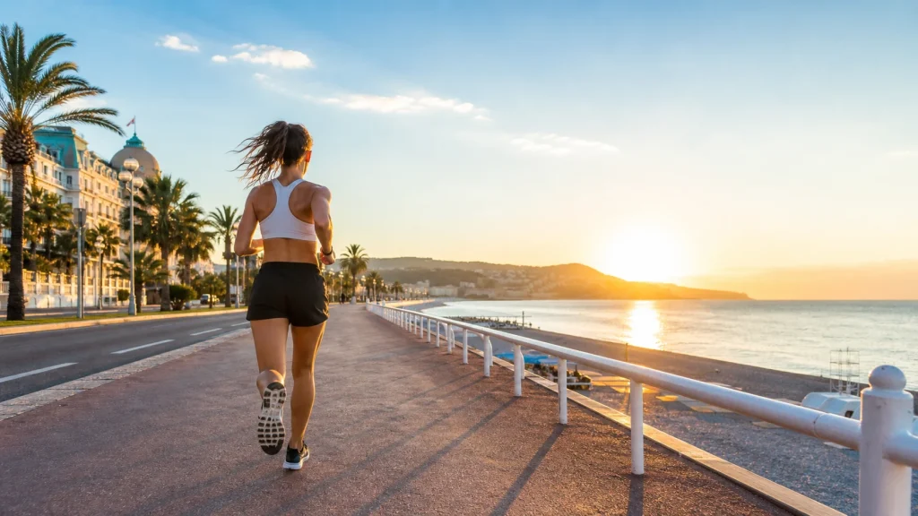 Coureuse sur la Promenade des Anglais à Nice au lever du soleil, avec la mer Méditerranée et les palmiers en arrière-plan.
